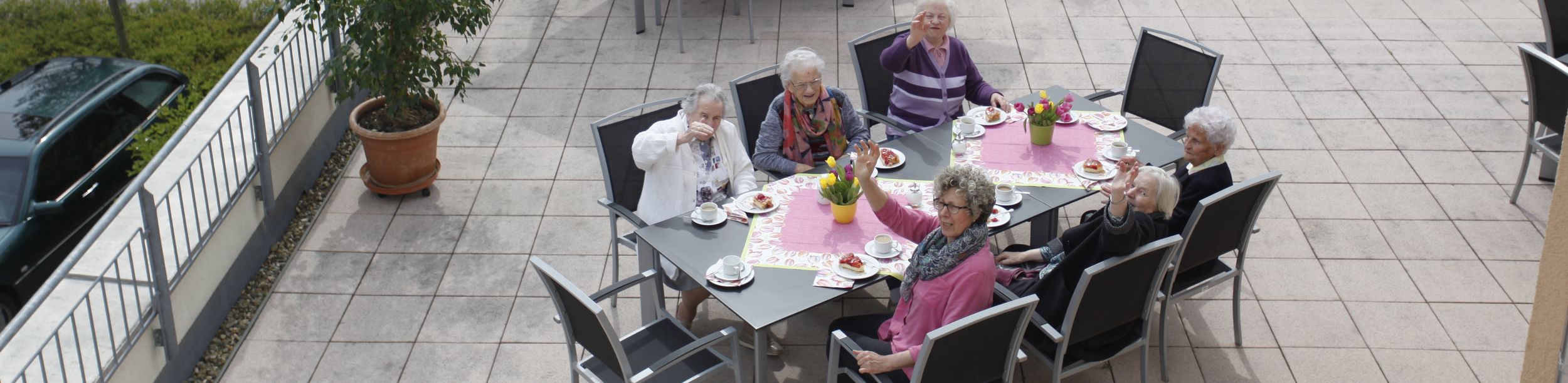 Ältere Menschen bei Kaffeetafel auf Terrasse, einige winken