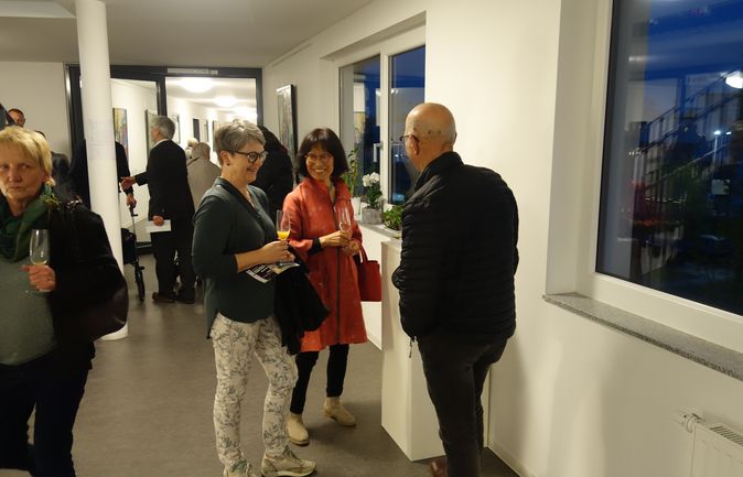Drei Personen unterhalten sich mit Getränken bei Vernissage