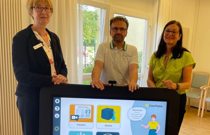 Drei Mitarbeitende stehen hinter einem CareTable Touchscreen im Seniorenzentrum