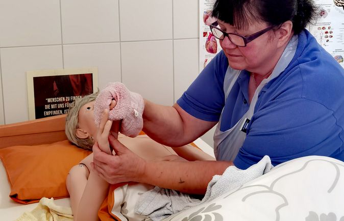 Pflegekraft legt Waschlappen ans Gesicht einer Übungspuppe im Pflegeübungsraum